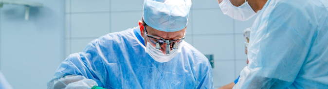 A surgeon wearing surgical glasses and a nurse