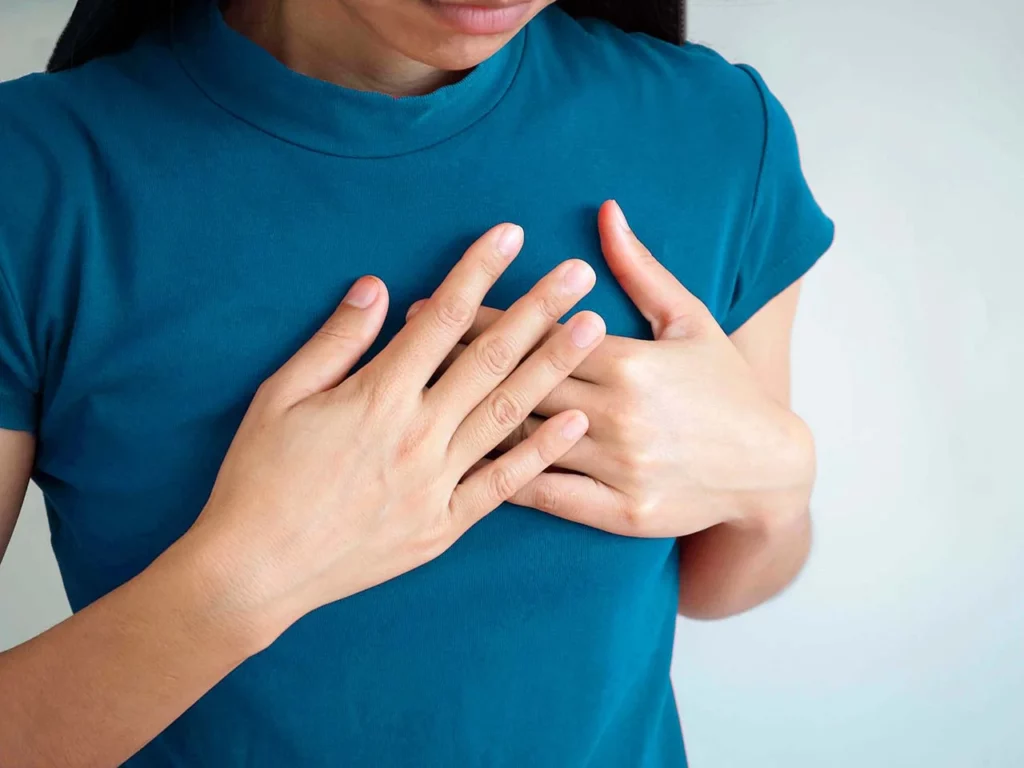 Mujer con las manos en el pecho debido a una fibrilación ventricular, causas.