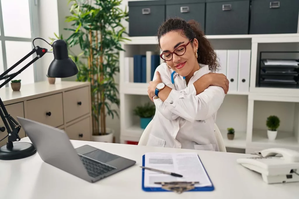 Joven doctora abrazándose feliz en el horario laboral.