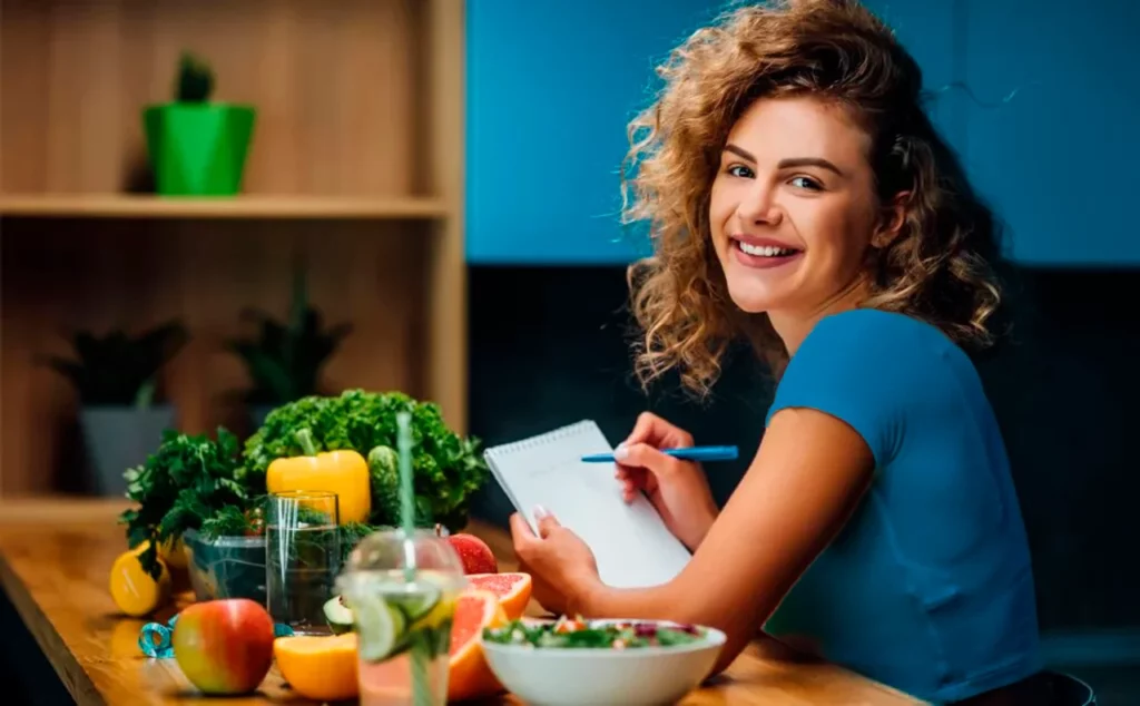 Nutricionista sentada frente a diversos alimentos redactando diferentes tipos de dietas para sus pacientes.