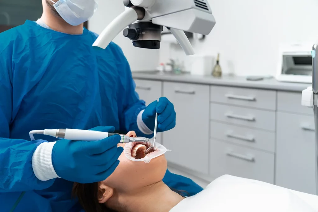 Dentista realizando un procedimiento de endodoncia a una paciente que está en la silla de su consultorio.
