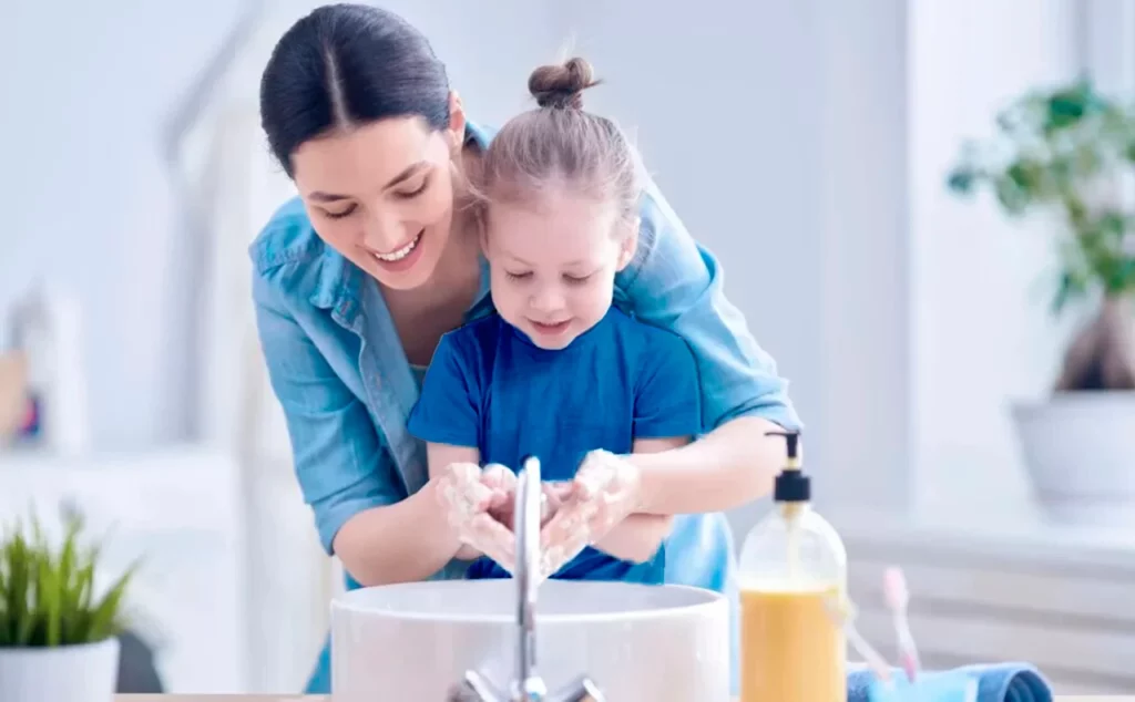 Una madre le explica a su hija los diferentes hábitos de higiene para niños mientras le ayuda a lavarse las manos.
