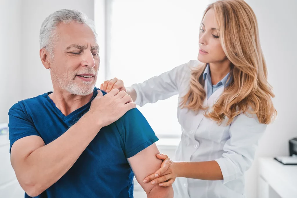 Doctora revisando a su paciente por lesión que es una luxación de hombro y le causa dolor.