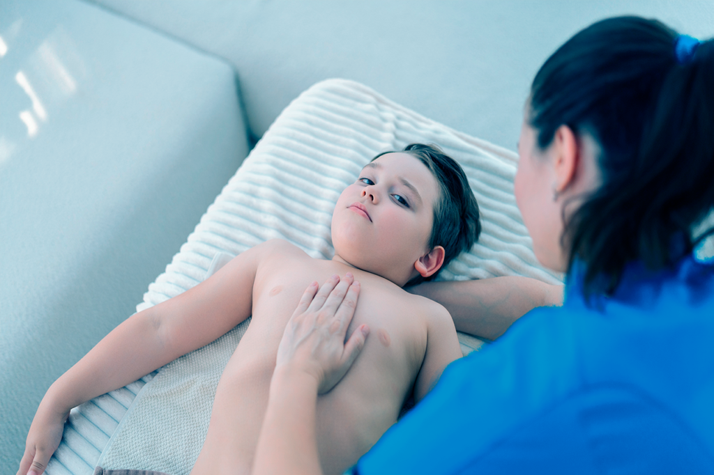 Niño con pecho de paloma que está acostado y siendo revisado por su doctora.