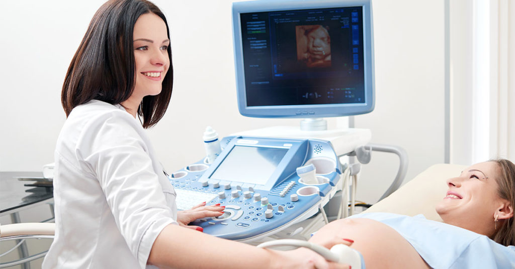 Mujer en su control prenatal, acostada mientras le realiza una especialista un ultrasonido.