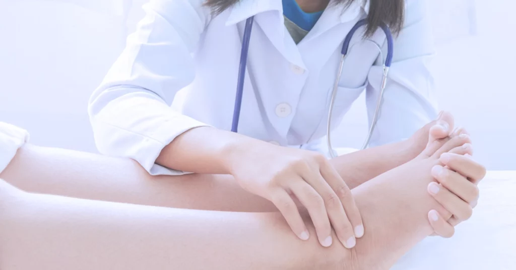 Doctora revisando por qué se hinchan los pies y duelen a un paciente en consulta.
