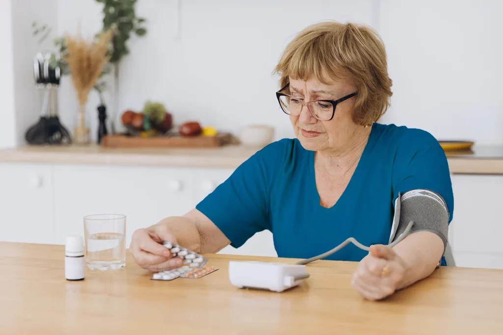 Mujer identificando cómo bajar la presión alta, mientras se mide la presión y se prepara para tomar sus medicamentos.