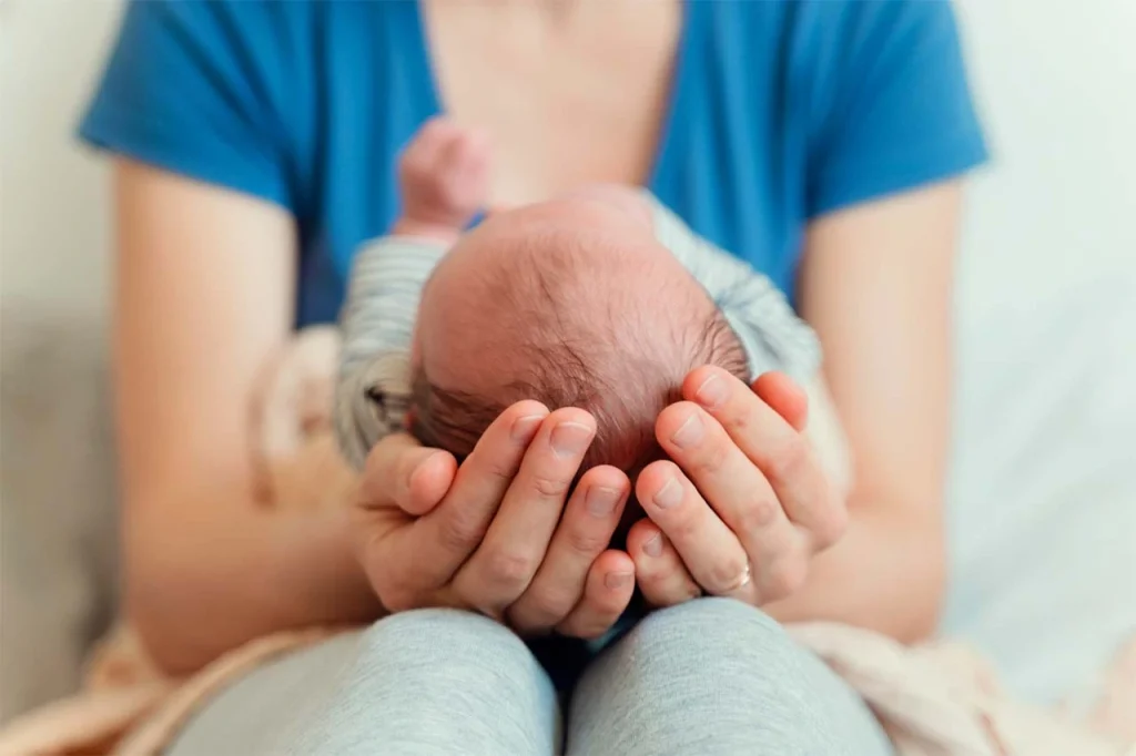 Mujer sostiene entre sus manos la cabeza de su bebé, tras un parto humanizado, después de que éste haya nacido. Mujer sostiene entre sus manos la cabeza de su bebé, tras un parto humanizado, después de que éste haya nacido.