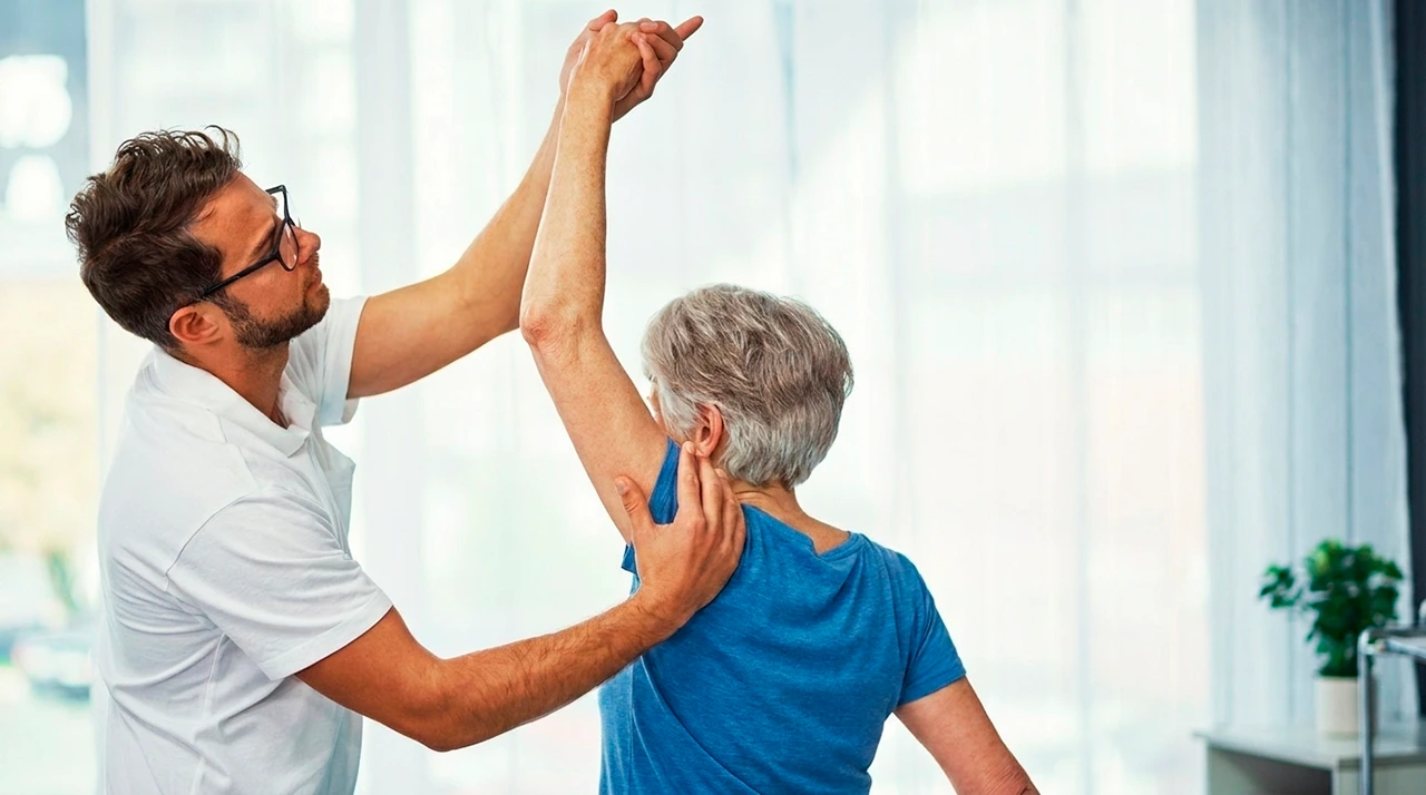 Paciente con mialgia, realizando fisioterapia, donde el especialista le ayuda a estirar el brazo hacia arriba.
