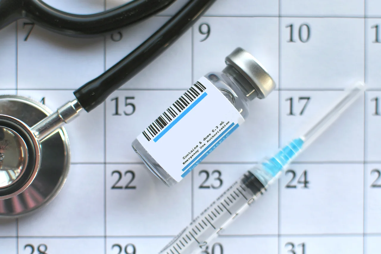 Frasco, jeringa y calendario para representar lo que engloba la cartilla de vacunación.