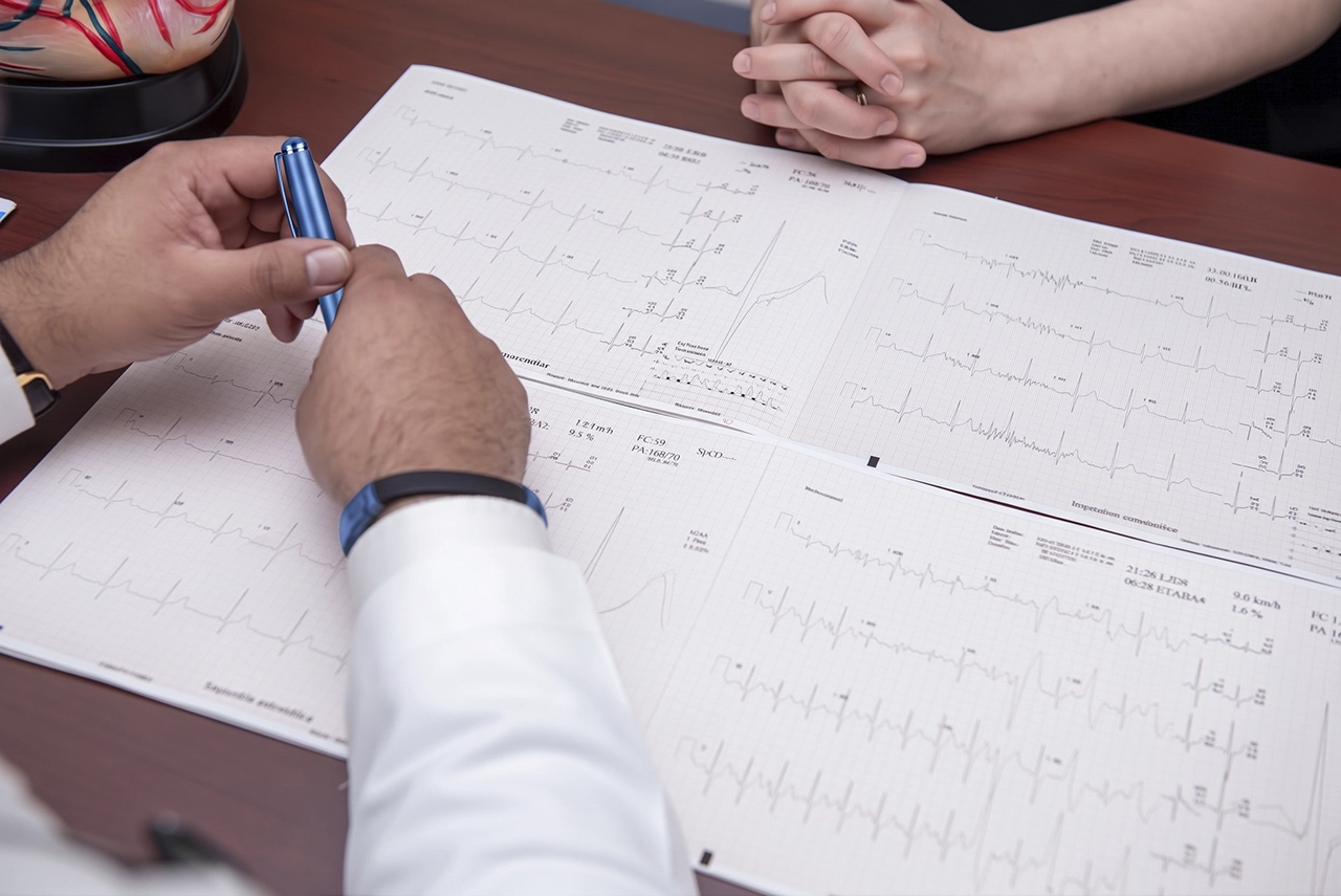 Especialista leyendo los resultados de un electrocardiograma, durante una consulta, la impresión está sobre un escritorio.